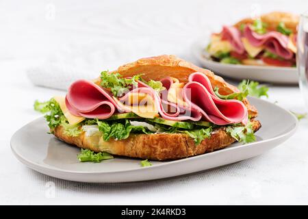 Croissant o sandwich freschi con insalata, prosciutto e formaggio su sfondo chiaro. Foto Stock