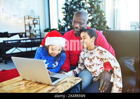 la famiglia afro-americana effettua una videochiamata tramite un computer portatile e comunica con i parenti alla vigilia di capodanno sullo sfondo del natale Foto Stock