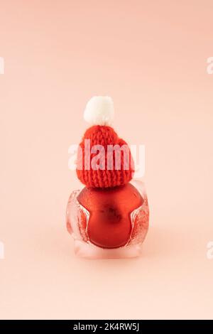 Rosso Natale babble con cappello di Babbo Natale in cubo di ghiaccio in fusione su sfondo rosa. Biglietto di auguri per il nuovo anno. Concetto minimo. Foto Stock