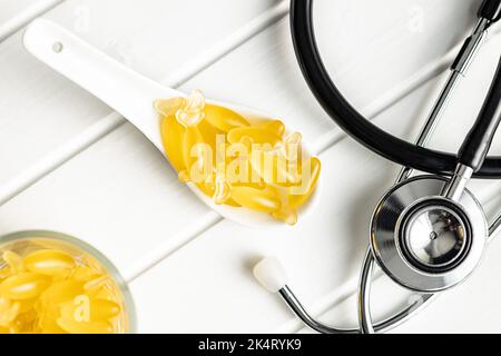 Capsule di olio di pesce. Omega 3 pillole gialle in cucchiaio sul tavolo bianco. Vista dall'alto. Foto Stock