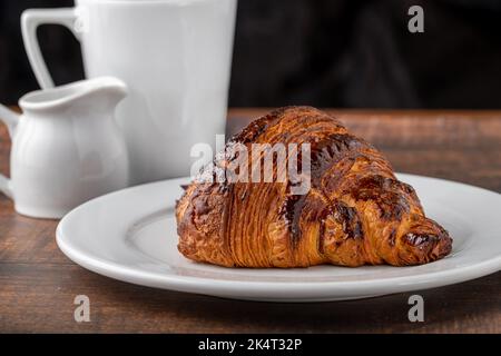 Croissant con caffè a fianco su un tavolo di legno Foto Stock