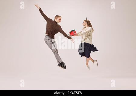 Ballerini flessibili, giovane coppia felice in abiti caldi d'inverno ballando con scatole regalo festive su sfondo grigio. Buon Natale, Capodanno, vacanze Foto Stock