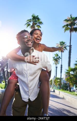 Allegro verticale ritratto di una giovane coppia di gara mista facendo piggyback in vacanza su un'isola. Foto Stock