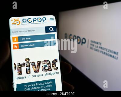Persona che tiene il cellulare con il sito web dell'autorità italiana per la protezione dei dati (GPDP) sullo schermo davanti al logo. Messa a fuoco al centro del display del telefono. Foto Stock
