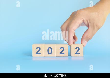 Anno 2022 fine, conclusione e finalizzazione del concetto. Mano umana completa blocchi di legno su sfondo blu. Foto Stock