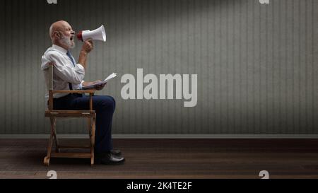 Regista professionista e sicuro seduto sulla sedia del regista e gridando con un megafone, concetto di industria cinematografica Foto Stock