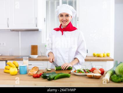 Donna proffesional cuoca in bianco uniforme tagliando verdure Foto Stock