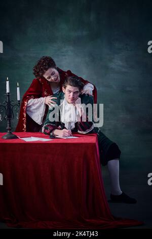 Ritratto di donna a immagine di vampiro che vuole mordere il collo dell'uomo su sfondo verde scuro. Uomo scrivere lettera Foto Stock