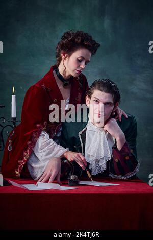 Ritratto di uomo e donna in costumi medievali su sfondo verde scuro. Scrivere una misteriosa storia sui vampiri Foto Stock