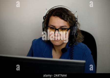 Un operatore di call center serio sta parlando con un cliente mentre guarda lo schermo di un computer in primo piano. Un telemarketing, un agente di telemarketing, fa un c Foto Stock