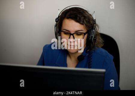 Un operatore di call center serio sta parlando con un cliente mentre guarda lo schermo di un computer in primo piano. Un telemarketing, un agente di telemarketing, fa un c Foto Stock