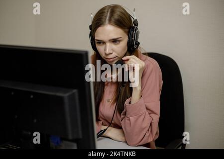 Un operatore di call center serio sta parlando con un cliente mentre guarda lo schermo di un computer in primo piano. Un telemarketing, un agente di telemarketing, fa un c Foto Stock