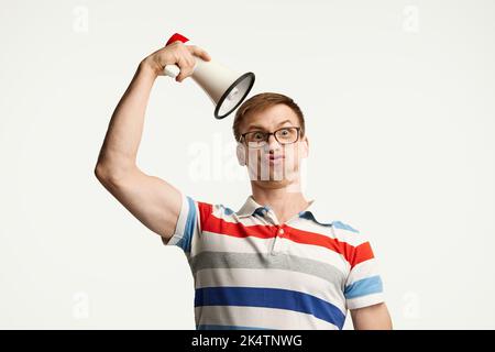 Ritratto di giovane uomo in vetro posato con megafone isolato su sfondo bianco studio. Aspetto divertente Foto Stock