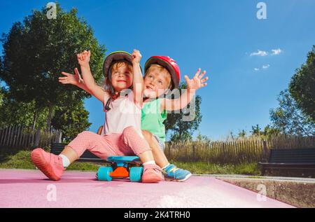 Due bambini piccoli giocano seduti sullo skate presso lo skatepark Foto Stock