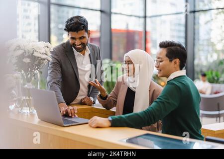 Un gruppo eterogeneo di persone aziendali si riunisce intorno a un notebook in un ufficio moderno Foto Stock
