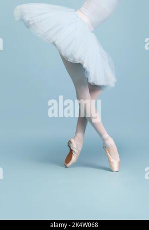 Immagine ritagliata di gambe femminili, ballerina in tutu e punta in piedi sulla punta isolata isolato su sfondo blu studio Foto Stock