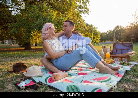 Coppia abbracciata seduta su coperta intento sul pic-nic vegan guarda gli occhi di ciascuno con amore. Foto Stock