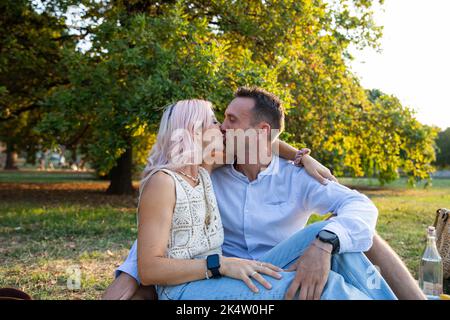 Coppia amorevole seduta sull'erba nel parco bacia appassionatamente in bocca. Foto Stock
