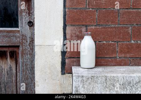 Una pinta piena di latte fresco, in una bottiglia di vetro, lasciata all'esterno di una casa dal milkman locale. Il biberon è sormontato da un foglio di alluminio sicuro Foto Stock