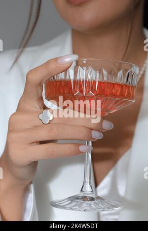 Immagine verticale di una femmina caucasica che tiene un bicchiere da cocktail con un anello sul dito Foto Stock