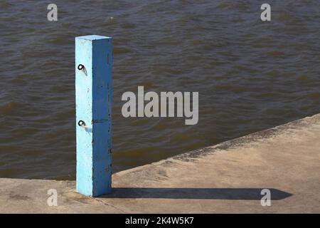 Palo per calcestruzzo con catene ganci su molo, palo per molo blu, pilastri per molo in cemento blu con luce solare. Foto Stock