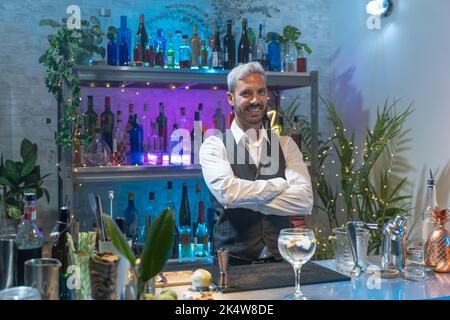 Ritratto di barman in una camicia bianca e grembiule nero sorridente guardando alla macchina fotografica alla festa in nightclub. Vita notturna. Foto Stock