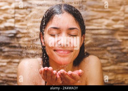Felice donna biraciale che prende la doccia, lavando i capelli in bagno Foto Stock