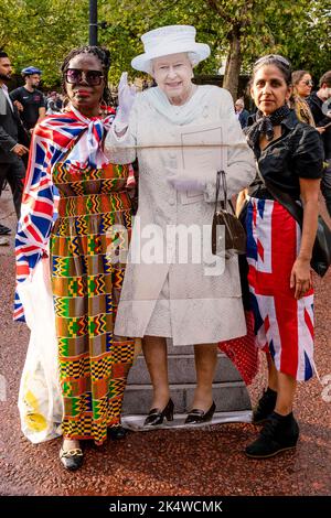 Il giorno dopo la morte della Regina Elisabetta II due donne portano Con sé Un taglio di cartone a grandezza naturale della Regina in Tribute, The Mall, Londra, Regno Unito. Foto Stock