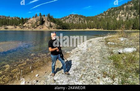 Fotografo in piedi sulla spiaggia utilizzando un teleobiettivo, Okanagan, British Columbia, Canada Foto Stock