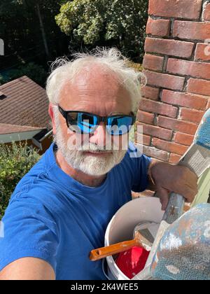 Ritratto di un uomo anziano in piedi su una scala che dipinge una casa, British Columbia, Canada Foto Stock