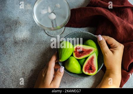 Vista dall'alto di una donna che tiene una ciotola di fichi verdi maturi e un bicchiere di acqua ghiacciata Foto Stock