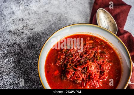 Vista dall'alto di una ciotola di zuppa tradizionale Ucraina di barbabietole (borscht) su un tavolo con un cucchiaio e tovagliolo Foto Stock