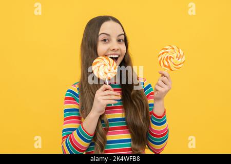 Bambino teen freddo con lollipop sopra sfondo isolato giallo. Dolce vita d'infanzia. Ragazza teen con caramella lollipop yummy. Foto Stock