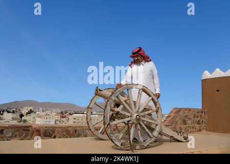 Uomo arabo che ispeziona vecchio cannone su A'Arif Fort tetto top Hail Arabia Saudita Foto Stock