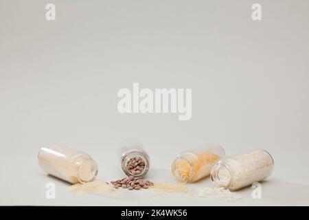vasetti di vetro senza tappo sdraiati sul tavolo, lenticchie, pasta e riso, fondo morbido verdastro Foto Stock