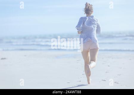 Visto da dietro donna di mezza età alla spiaggia che corre. Foto Stock