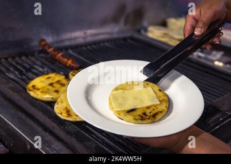 Primo piano delle mani mettere un'arepa con formaggio su un piatto bianco Foto Stock