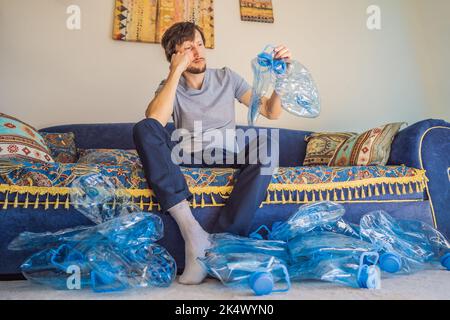 Il giovane uomo caucasico ha tra bottiglie di plastica vuote da riciclare con triste espressione Foto Stock