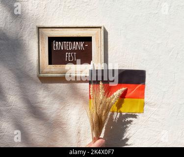 Happy Germany Thanksgiving Day o Erntedankfest in lingua tedesca. Bandiera tedesca e mazzo di spighe di grano su tessuto beige. Piano di giacitura, vista dall'alto. Foto Stock