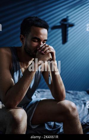 Insomniac ragazzo con medaglioni metallici in mani in preghiera nel cuore della notte, mentre rimanere sveglio e soffrire di PTSD Foto Stock