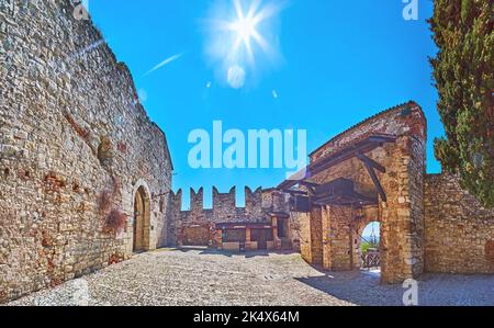 Panorama del cortile medievale in pietra del Castello di Brescia con mura, merli e la porta conservati, Italia Foto Stock