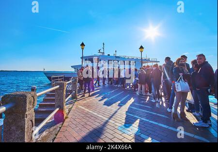 SIRMIONE, ITALIA - 10 APRILE 2022: La linea di peope sul molo al traghetto sul Lago di Garda al tramonto, il 10 aprile a Sirmione Foto Stock