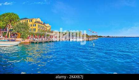 Il molo dei traghetti sul Lago di Garda osserva le case colorate lungo la banchina, Piazza Giosue Carducci, le barche ormeggiate e il tramonto sul traghetto, Sirmione, Ita Foto Stock