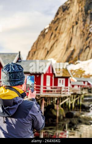 Vista posteriore del turista fotografando le cabine rosse di Rorbu nel villaggio di pescatori di Reine, Isole Lofoten, contea di Nordland, Norvegia Foto Stock