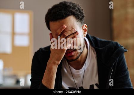 Giovane depresso uomo che tocca il viso mentre soffre di sindrome post traumatica e descrive i suoi problemi a sessione psicologica Foto Stock