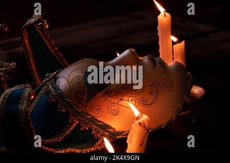 La maschera veneziana si trova su un tavolo di legno con candele, maschera e candele Foto Stock