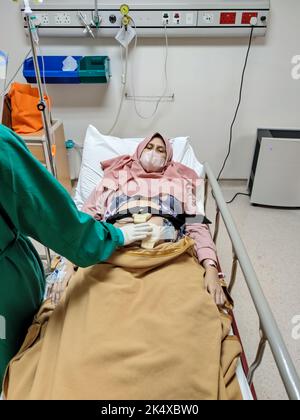 Paziente adagiato sul letto che riceve cure mediche da infermiera con uniforme verde nella stanza dell'unità di terapia intensiva in ospedale. Foto Stock