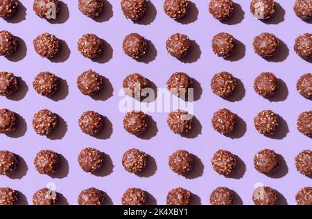 Fondo a cornice con molti tartufi di cioccolato allineati simmetricamente su un tavolo viola. Caramelle al cioccolato e alle nocciole in luce brillante su una vibra Foto Stock
