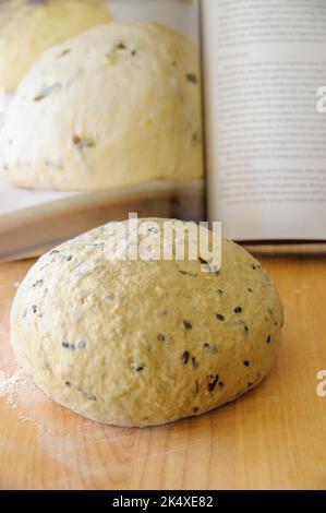 una palla di pasta di pane artissinale su un pannello di legno con un libro di ricette sfocato sullo sfondo Foto Stock