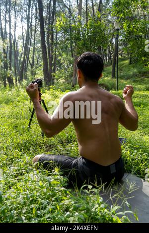 Ragazzo millenario meditando con l'allenatore online tramite la connessione iPad tablet, nella foresta, trasmettendo online la tua classe e le istruzioni, messico Foto Stock